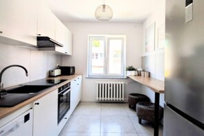 A modern kitchen with white cabinetry, a black countertop, a built-in oven, a microwave, and a window with a view of the outside. - Large Holiday Apartment With Sauna (Kołobrzeg)