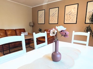 A dining area with a white table, a vase with flowers, and framed artwork on the wall.