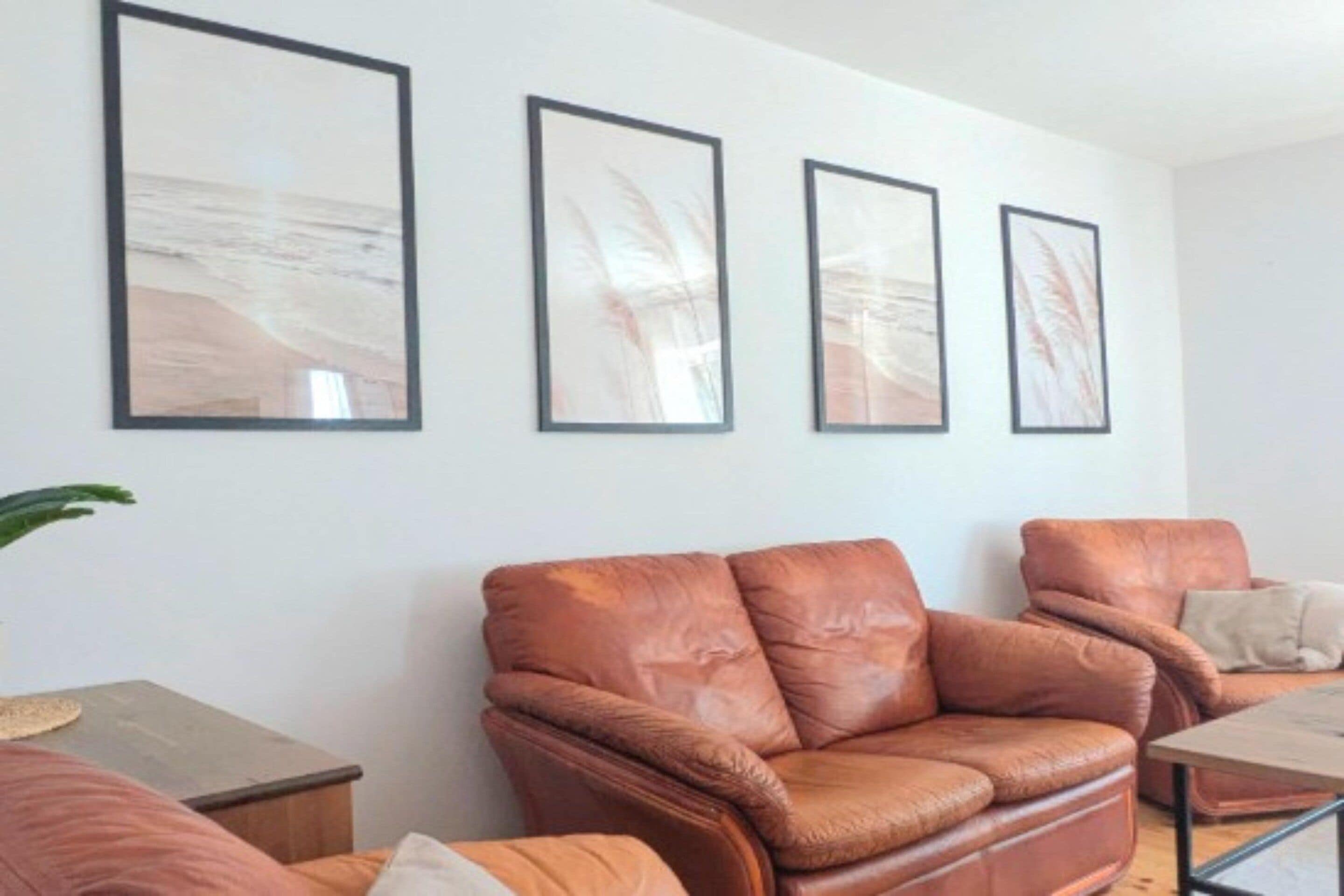 A living room with a brown leather sofa, a small table, and three framed abstract paintings on the wall.