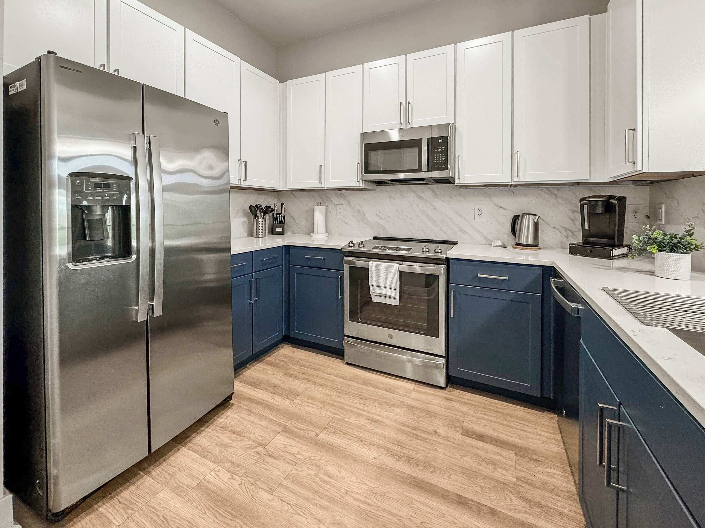 A modern kitchen with stainless steel appliances, white cabinets, and a wooden floor.