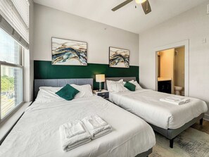 A hotel room with two beds, a large window, artwork on the walls, and a bathroom visible through an open door. - Luxury 2BD | Deep Ellum | Parking | Pool+Gym (Dallas)