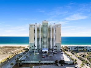 A high-rise hotel with a central atrium, a parking lot, and a view of the beach and ocean.
