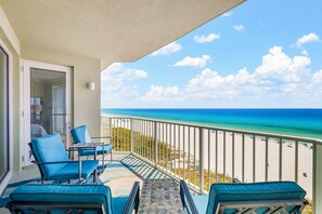 A balcony with blue chairs and a table, overlooking a beach with clear blue water and white sand. - NEW Boardwalk Beachfront 603 Updated, Heated Pool, Hot Tub, FREE GOLF & PERKS (Panama City Beach)