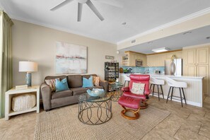 A living room with a sofa, a red chair, a glass coffee table, and a kitchen in the background. - NEW Boardwalk Beachfront 603 Updated, Heated Pool, Hot Tub, FREE GOLF & PERKS (Panama City Beach)