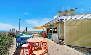 A beachside café with outdoor seating, a yellow awning, and a view of the ocean.