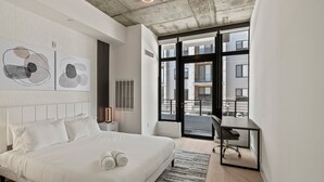 Ein modernes Schlafzimmer mit einem großen Bett, einem Schreibtisch und Blick auf die Stadt durch große Fenster.