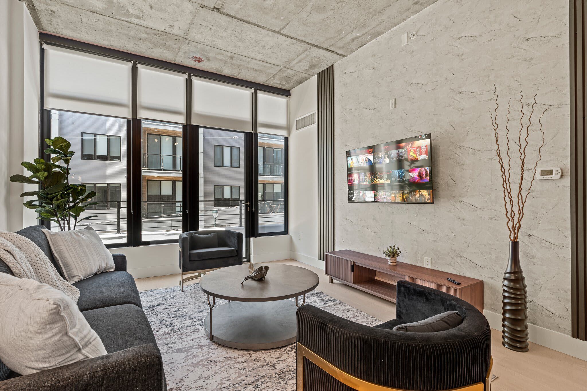 Una sala de estar moderna con sofá, sillón, mesa de centro y televisor montado en la pared.