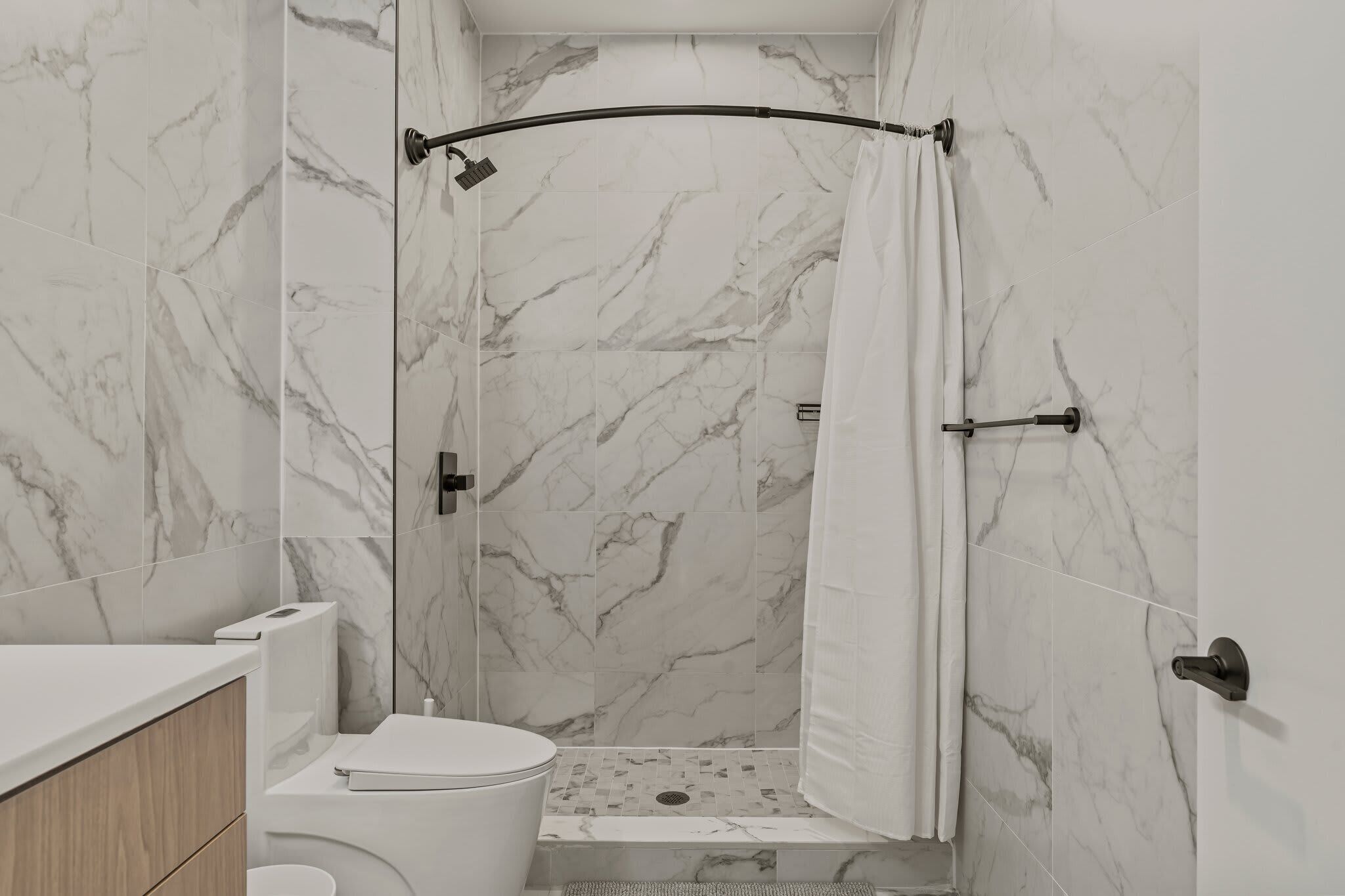Une salle de bain avec douche, toilettes et murs en marbre.