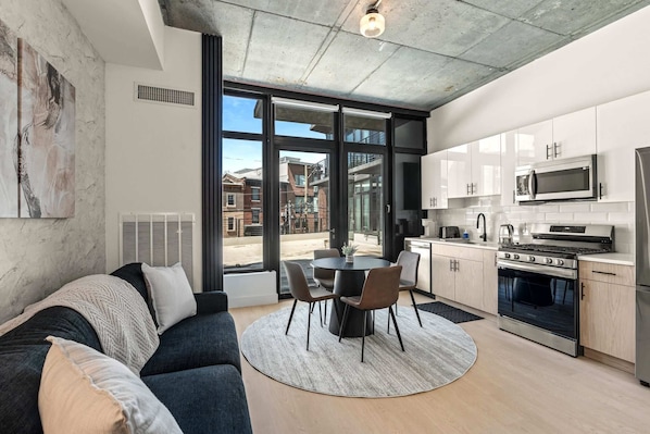 A modern kitchen with a dining area, large windows, and a view of buildings outside.