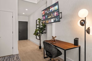 A modern interior with a flat-screen TV mounted on the wall, a desk with a chair, a potted plant, and a floor lamp.