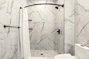 A modern bathroom with marble tiles, a shower with a curved door, and a toilet.