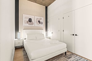 A modern bedroom with a large bed, white wardrobe, and abstract artwork on the wall.