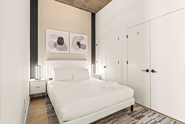A modern bedroom with a large bed, white wardrobe, and abstract artwork on the wall.