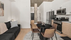 Eine moderne Küche mit Edelstahlgeräten, ein Essbereich mit rundem Tisch und Stühlen sowie ein Wohnbereich mit einer Couch und Kissen.