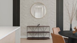 A modern dining area with a marble wall, a round mirror, a dark wooden console table, and a round table with chairs.