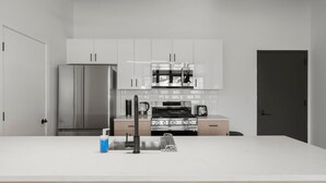 A modern kitchen with stainless steel appliances, white cabinetry, and a central island with a sink and faucet.