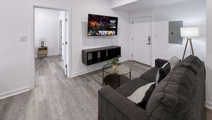 Un soggiorno moderno con una TV a schermo piatto, un divano, un tavolino da caffè e una lampada.