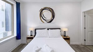 Una camera d'albergo con un letto grande, due comodini con lampade, un'opera d'arte a parete e una finestra con tende.