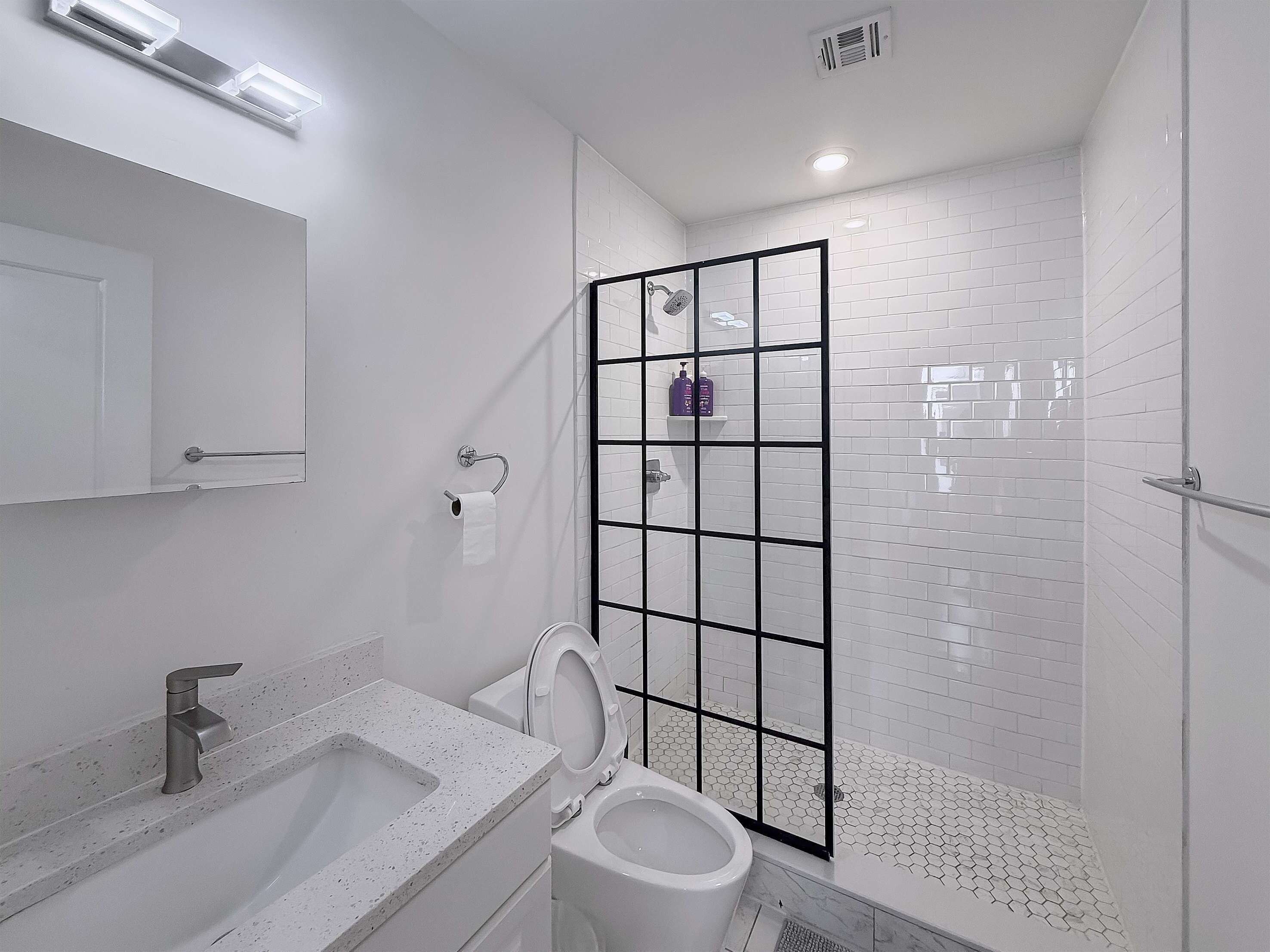 Un baño moderno con lavamanos, inodoro y zona de ducha blancos.