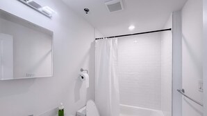 Un bagno moderno con lavabo, water, vasca e doccia, oltre a uno specchio sopra il lavabo.