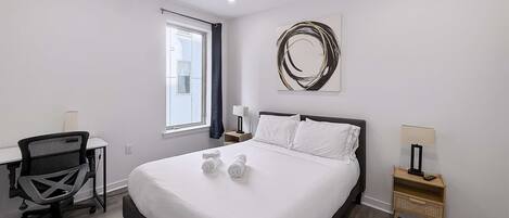 Een moderne hotelkamer met een bed, bureau, stoel en kunstwerk aan de muur.