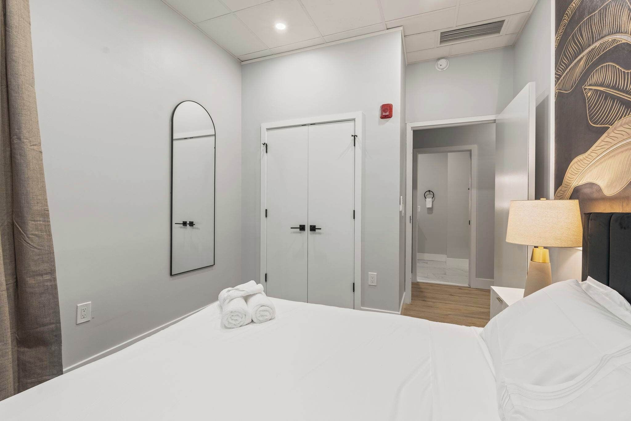 A hotel room with a large bed, a mirror, a wardrobe, and a lamp.