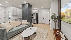 Una sala de estar moderna con un sofá gris, una mesa de centro de mármol y un ventanal con vistas a un bosque.