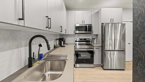 Una cocina moderna con electrodomésticos de acero inoxidable, armarios blancos y un fregadero grande.