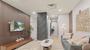 A modern living room with a wooden panel wall, a flat-screen TV, a marble pillar, a grey sofa, and a unique bamboo wall decoration.