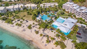 Vista aérea de un complejo turístico con una piscina grande, playa y varios edificios de hotel.