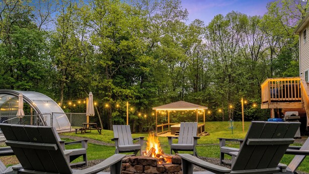 Un jardin avec un foyer, des fauteuils Adirondack, une table de pique-nique couverte et un barbecue.