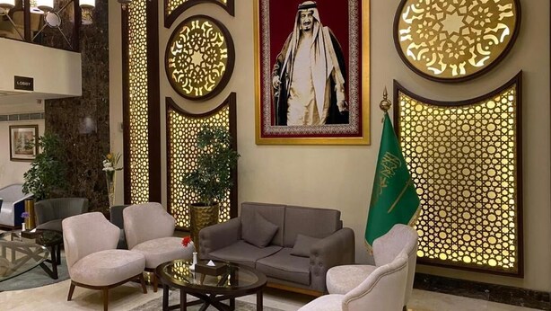 A lobby with a sofa, chairs, a coffee table, a framed portrait, and a flag. - ELITE PARK HOTEL (Jeddah)
