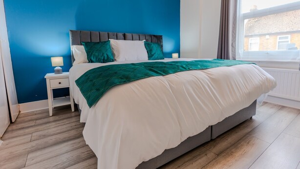 Une chambre à coucher avec un lit, une table de chevet, une fenêtre et une vue sur les bâtiments environnants.