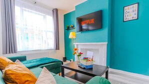 Un salon moderne avec des murs de couleur turquoise, un téléviseur à écran plat, une cheminée et une fenêtre avec des rideaux.