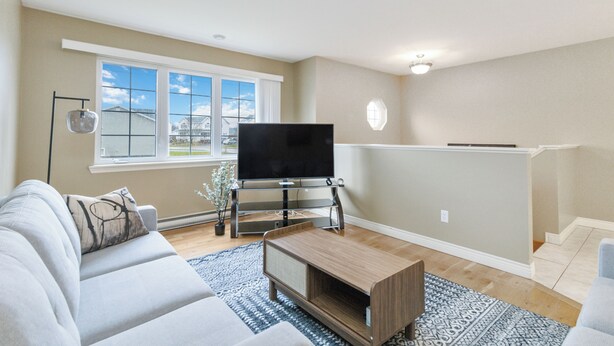 A living room with a sofa, a coffee table, a TV on a stand, a window, and a view of the outside. - Cozy, Comfortable and Spacious 2 Bedroom Home (Moncton)