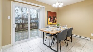 A dining area with a table set for four, a sliding glass door leading to a balcony, and a painting on the wall. - Cozy, Comfortable and Spacious 2 Bedroom Home (Moncton)