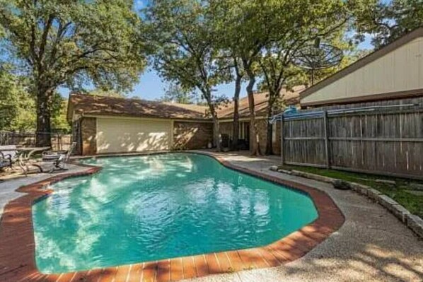 A rectangular swimming pool with a wooden deck edge, surrounded by trees and a covered patio area. - 3 Bedroom with a Pool (Bedford)