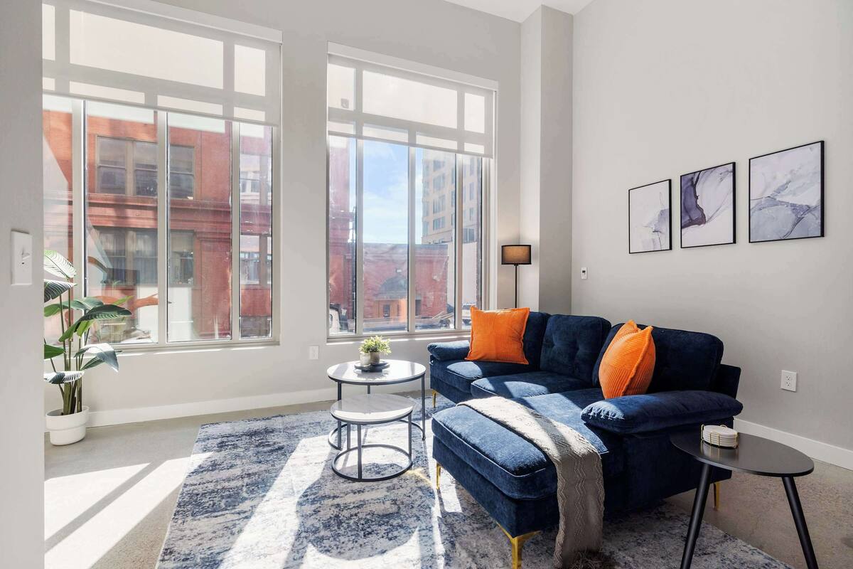 A modern living room with a blue sofa, a round coffee table, and a large window offering a city view.