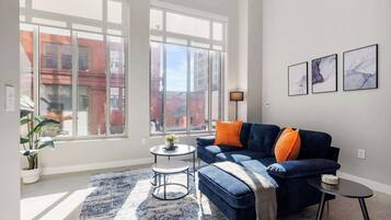 Una sala de estar moderna con un sofá azul, una mesa de centro redonda y un ventanal con vistas a edificios.