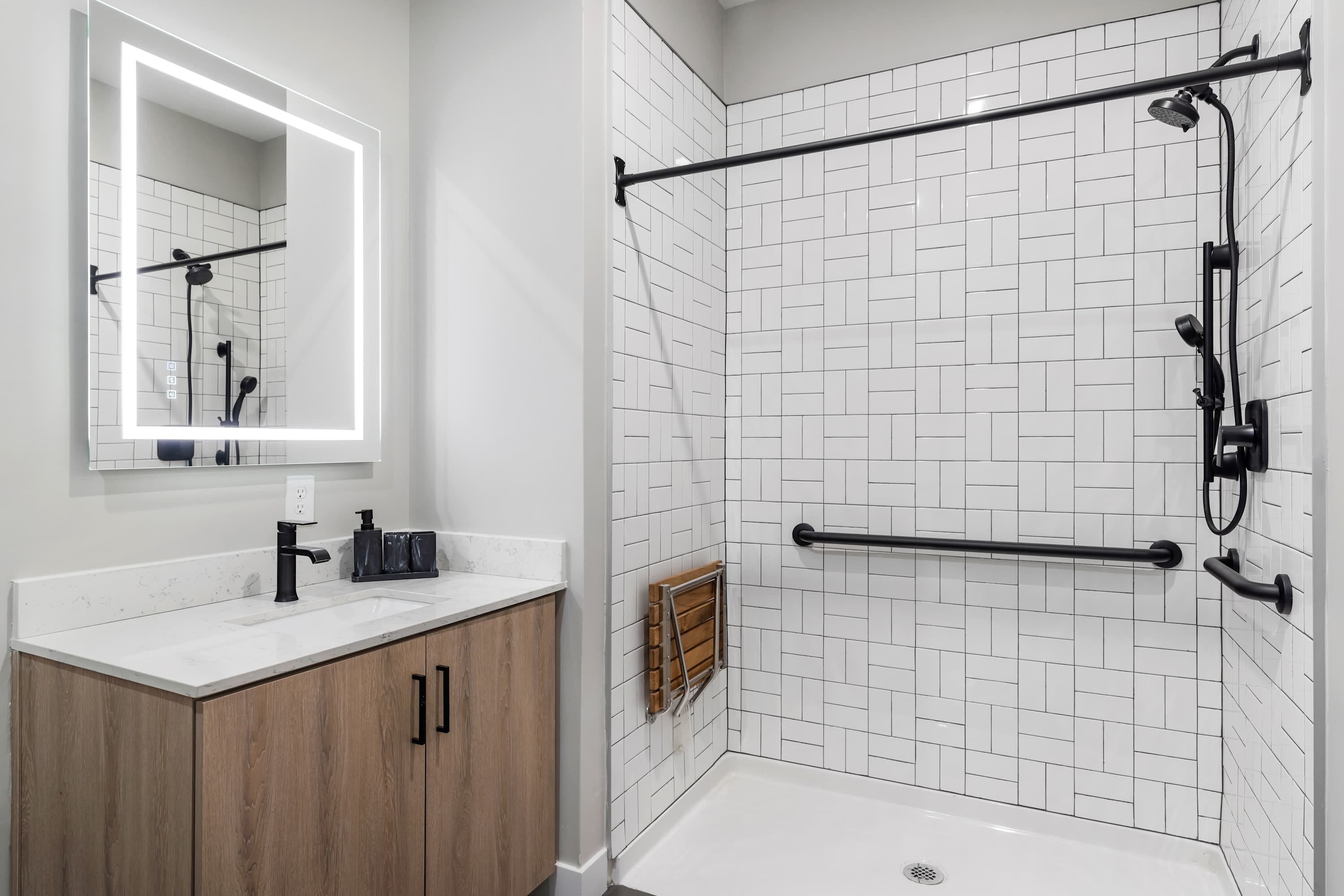 Un baño moderno con paredes de azulejos tipo metro blancos, un lavamanos blanco, armarios de madera, un perchero negro y un cabezal de ducha manual.