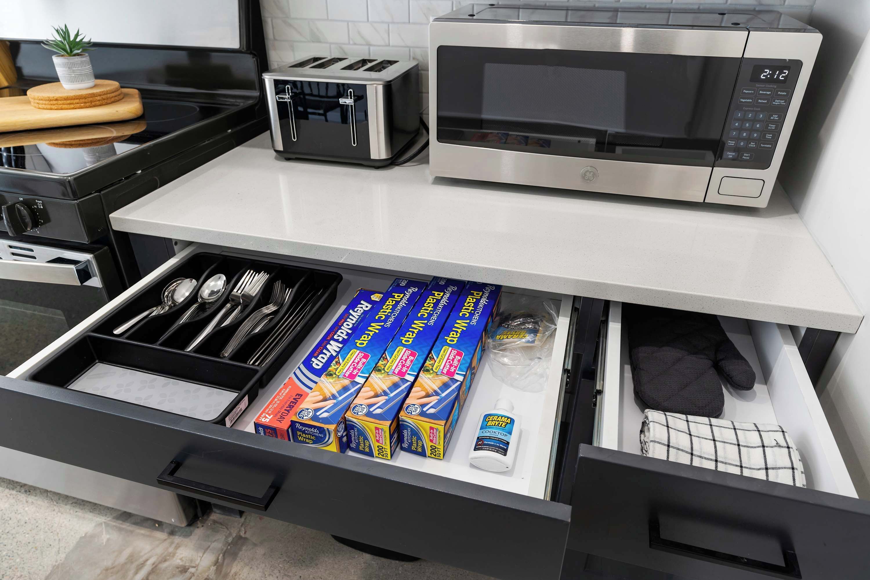 A kitchen with a microwave, toaster, and drawer containing utensils and cookware.