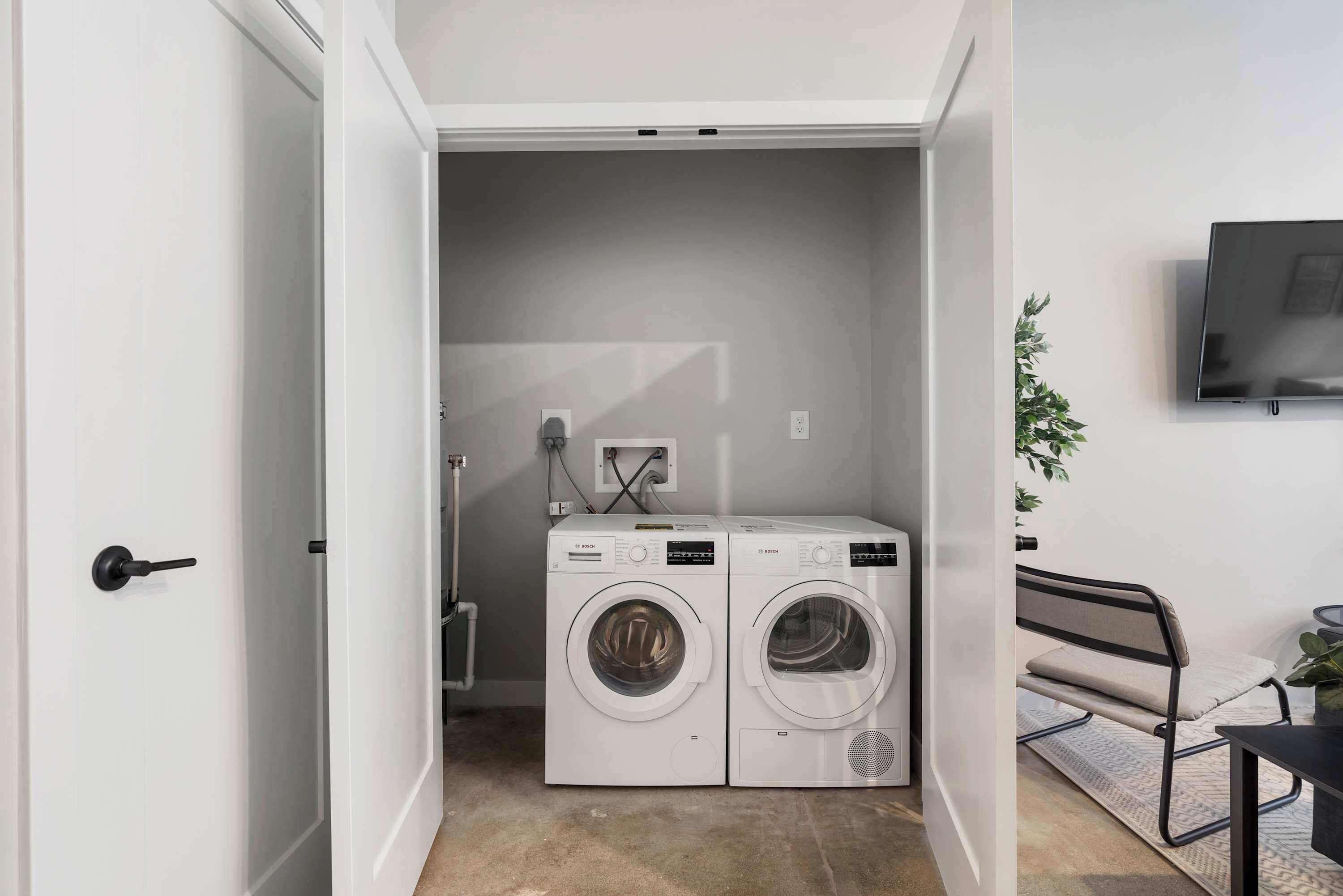 A laundry room with two front-loading washing machines, a wall-mounted TV, and a bench.