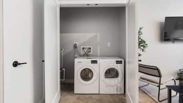 A laundry room with two front-loading washing machines, a wall-mounted TV, and a bench.