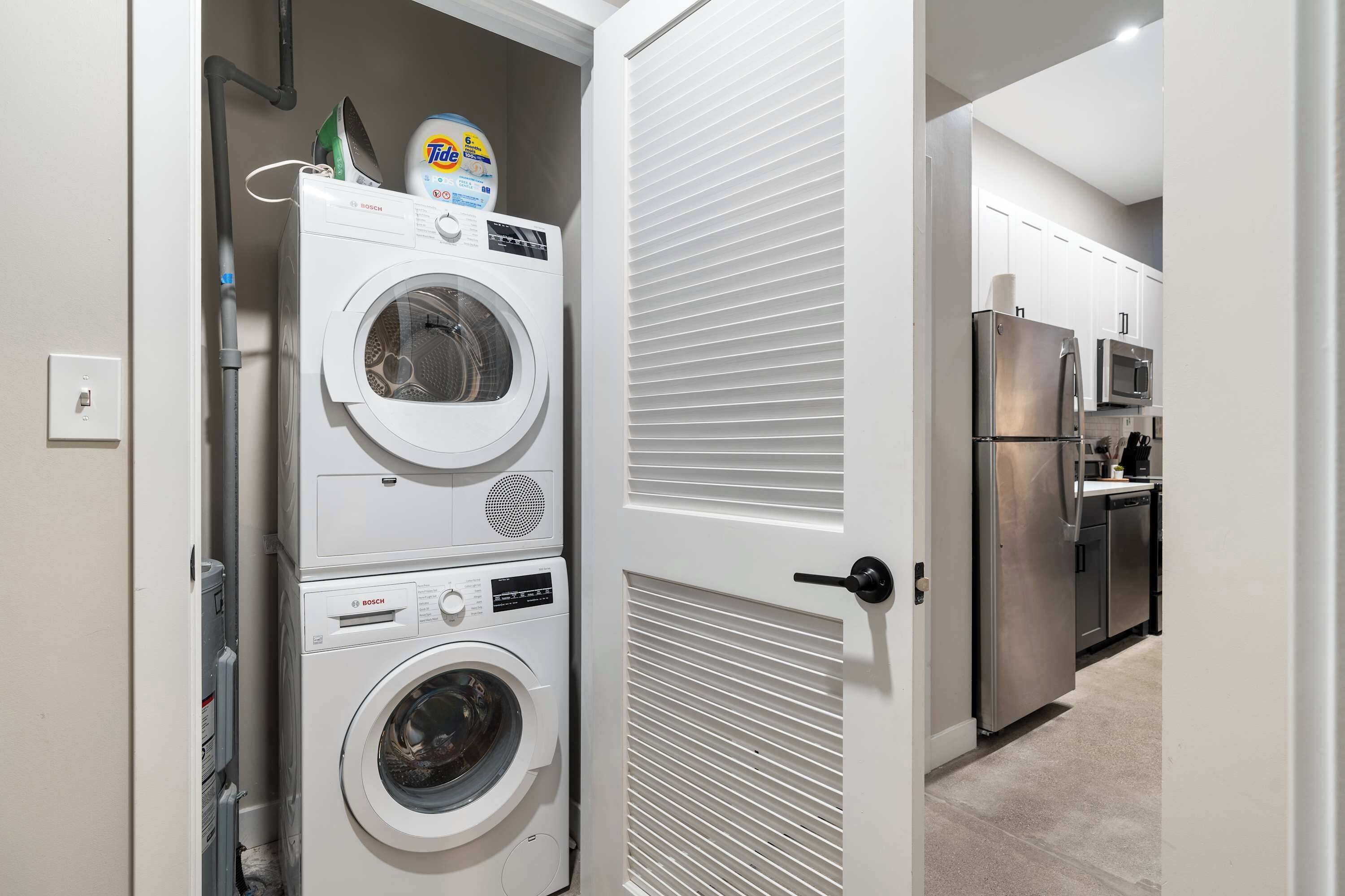 A laundry room with stacked washing machines and dryers, a refrigerator, and a microwave in the adjacent kitchen area.
