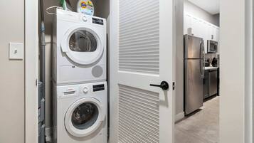 A laundry room with stacked washing machines and dryers, a refrigerator, and a microwave in the adjacent kitchen area.