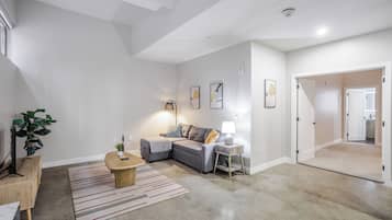 A modern living room with a grey sofa, a small wooden table, a lamp, and a plant.