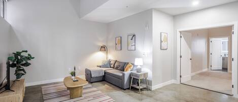 A modern living room with a grey sofa, a small wooden table, a lamp, and a plant.