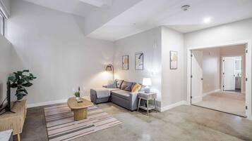 A modern living room with a grey sectional sofa, a wooden coffee table, and a striped rug. There is a lamp on a side table, and a plant in the corner.