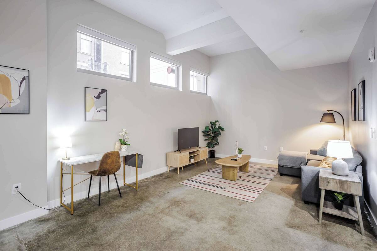 A modern living room with a white desk, a grey sofa, a TV, and a lamp.
