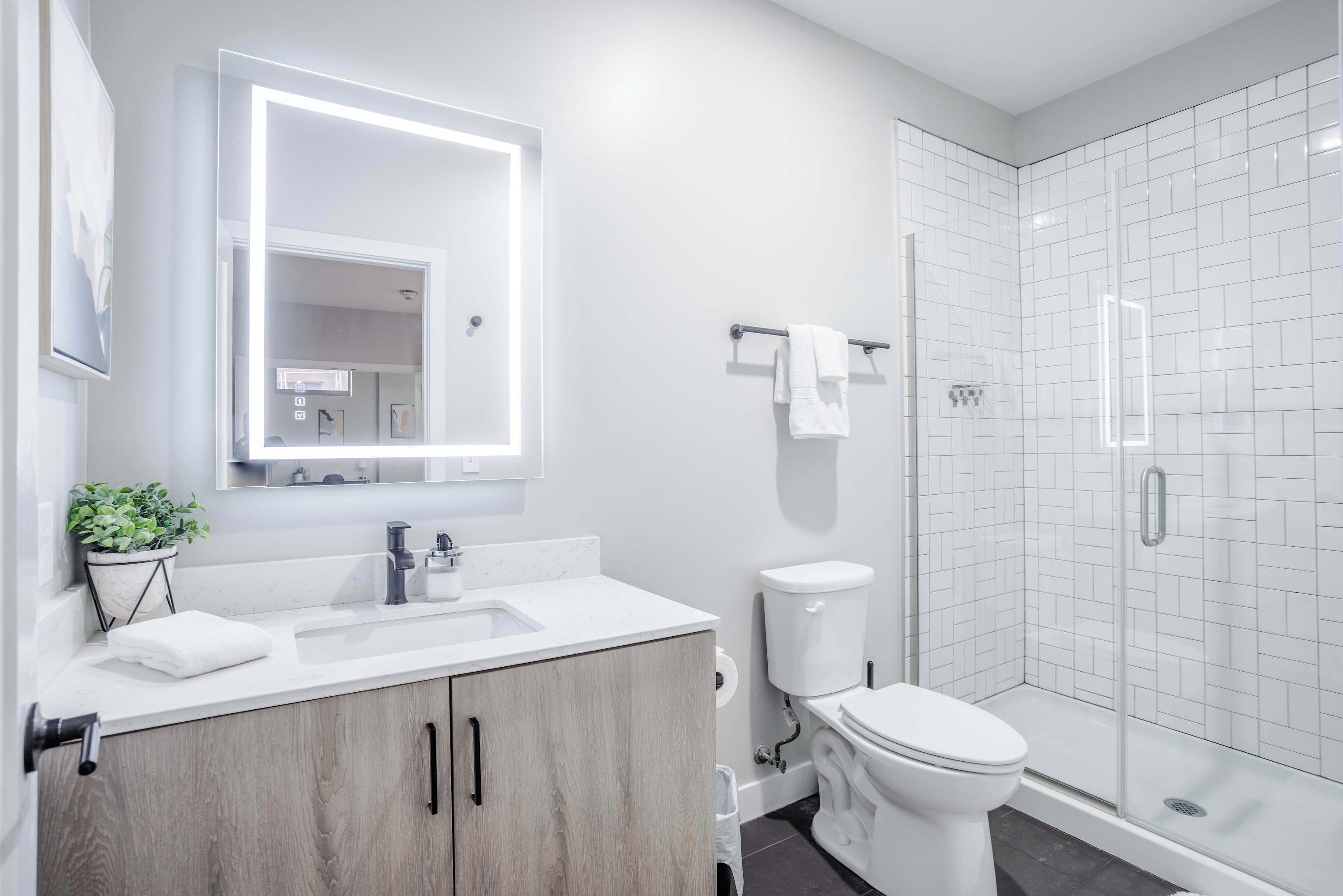 Ein modernes Badezimmer mit einem weißen Waschbecken, Holzschränken, einer Toilette und einer Duschkabine.
